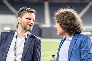 Two Men Standing Side By Side On A Grassy Field At NAB 2024